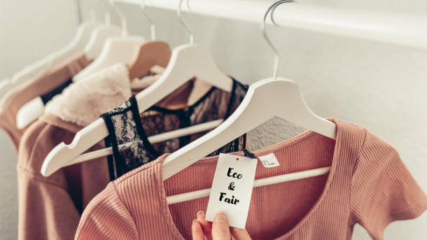 Kleidung hängt auf einem Kleiderständer, an einem der Kleidungsstücke hängt ein Etikett mit der Aufschrift "Eco & Fair"
