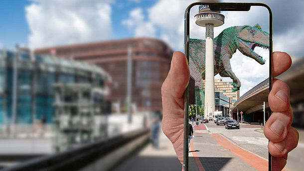 Eine Straße in Hannover. Davor hält eine Hand ein Handy. Auf dem Bildschirm ist ein Dinosaurier in der Szene zu sehen.